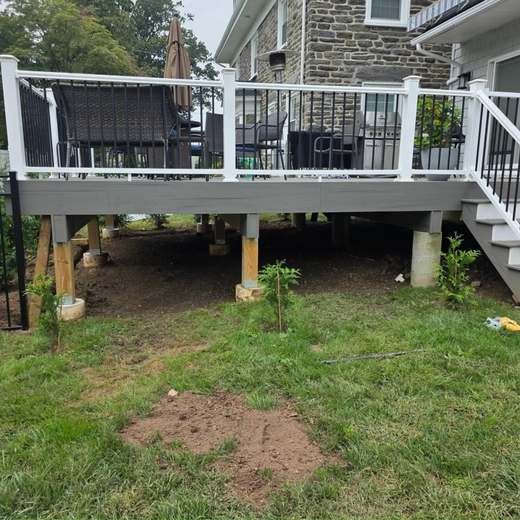 A white-railed composite deck built onto a Main Line stone house, with new footings and regraded lawn below.