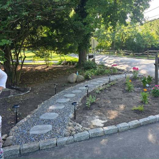 A curved flagstone stepping-stone path set in river stone, edged with granite cobble, running through a newly planted bed with path lighting.