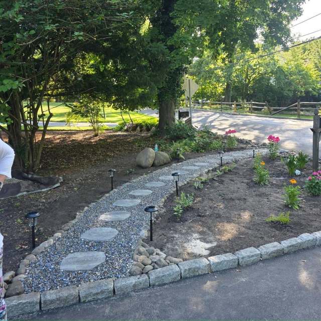 A curved flagstone stepping-stone path set in river stone, edged with granite cobble, running through a newly planted bed with path lighting.