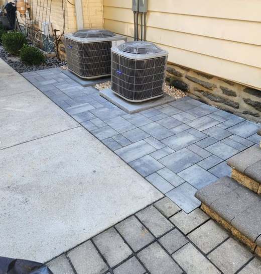 After: the same condensers standing on a level paver pad with a soldier-course border, tied into the concrete walk and the stone steps.