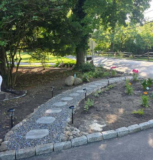 After: the same corner cleared and rebuilt as a stepping-stone path in river stone, with a granite cobble edge, new planting and path lights.