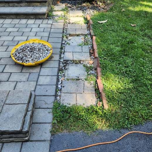 Before: old square stepping pavers sunk in weeds and gravel beside a paver walk, edged with loose brick along the lawn.