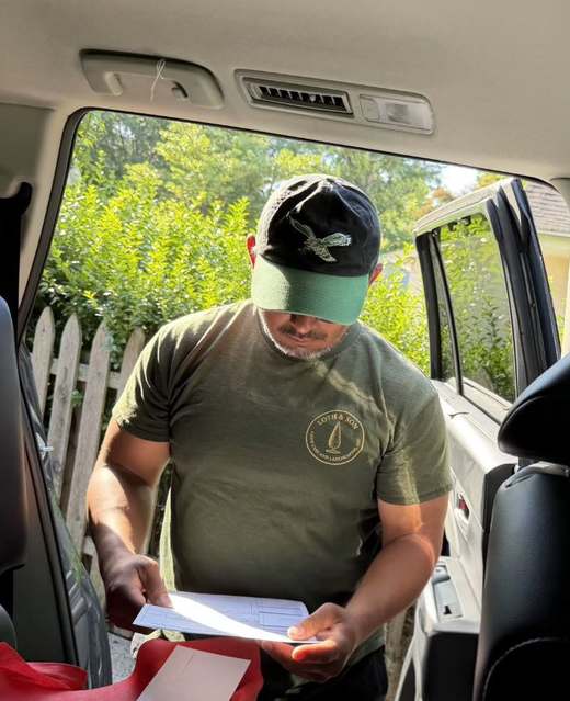 Rathana Yen in a Loth & Son branded shirt and cap, sitting in the open door of his truck reading a written work order on a clipboard.
