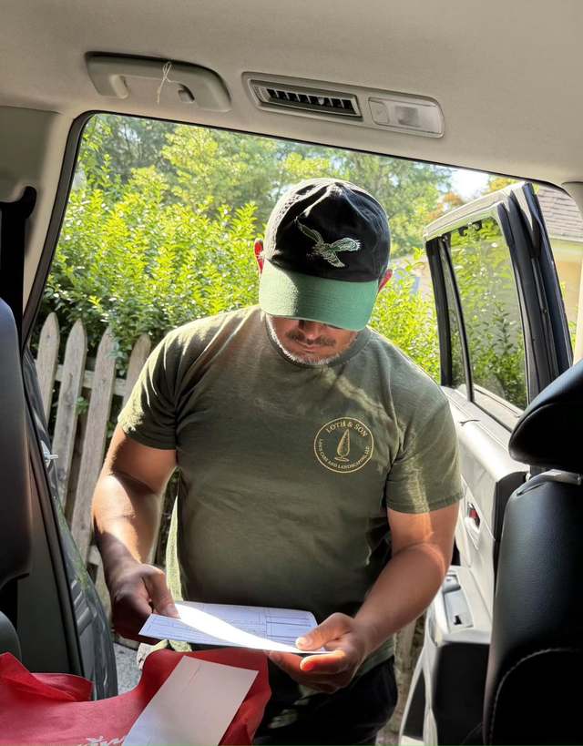 Rathana Yen standing at his truck in a Loth & Son shirt, reading through a written work order.