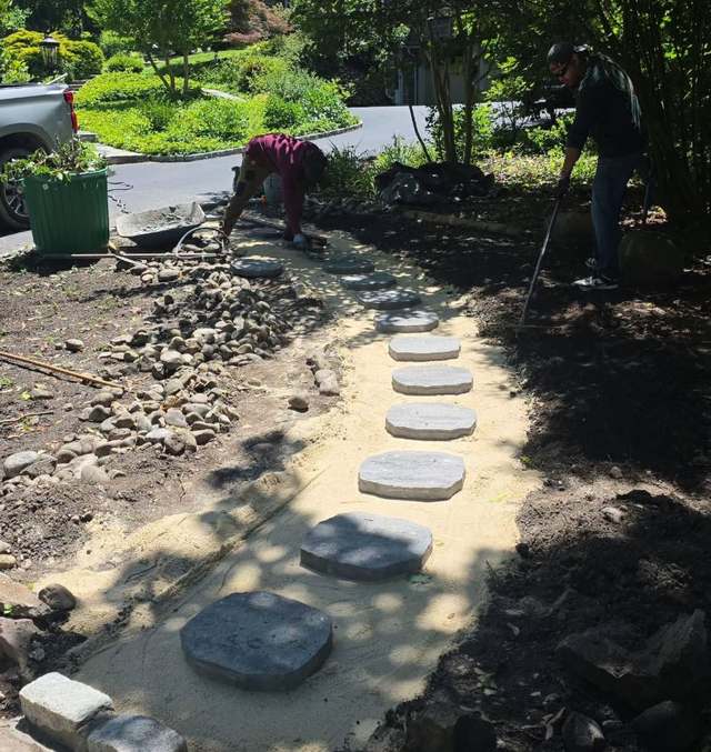Round stepping stones being set into a bed of sand and river stone mid-installation, with the surrounding ground still open.
